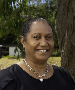 A smiling Aboriginal Woman pictured outside in nature wearing a black shirt and a silver necklace with love heart pendant