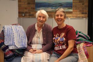 Zena seated with her daughter Gail surrounded by her crochet creations. Beautifully hand made crochet blankets. Stitched with love, kindness and care.